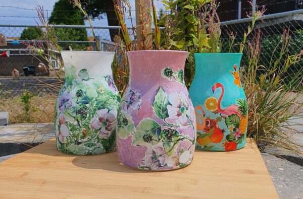Deelnemer bewerkt een vaas met decoupage tijdens een creatieve workshop, gebruikmakend van servetten en acrylverf.